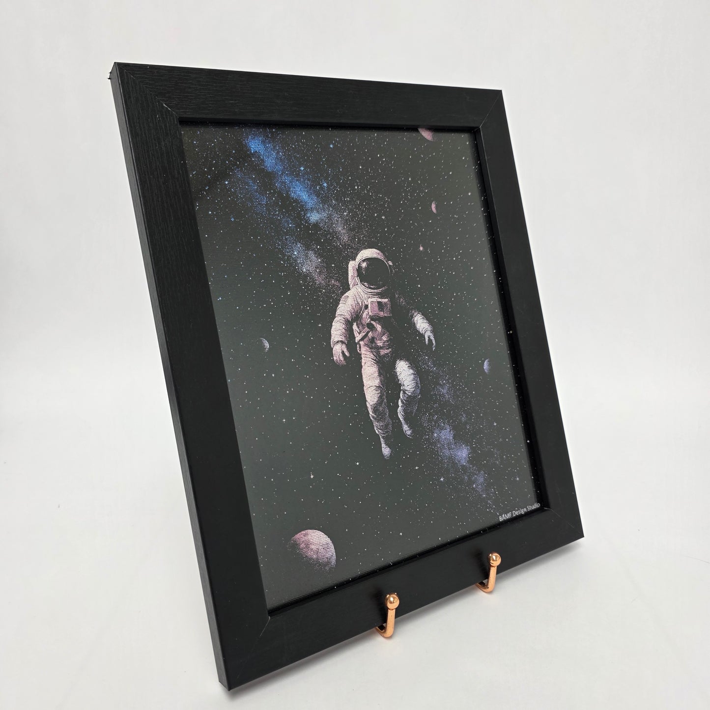 Black framed canvas print of an astronaut floating in space surrounded by stars and planets. Black, blue, and purple accents.