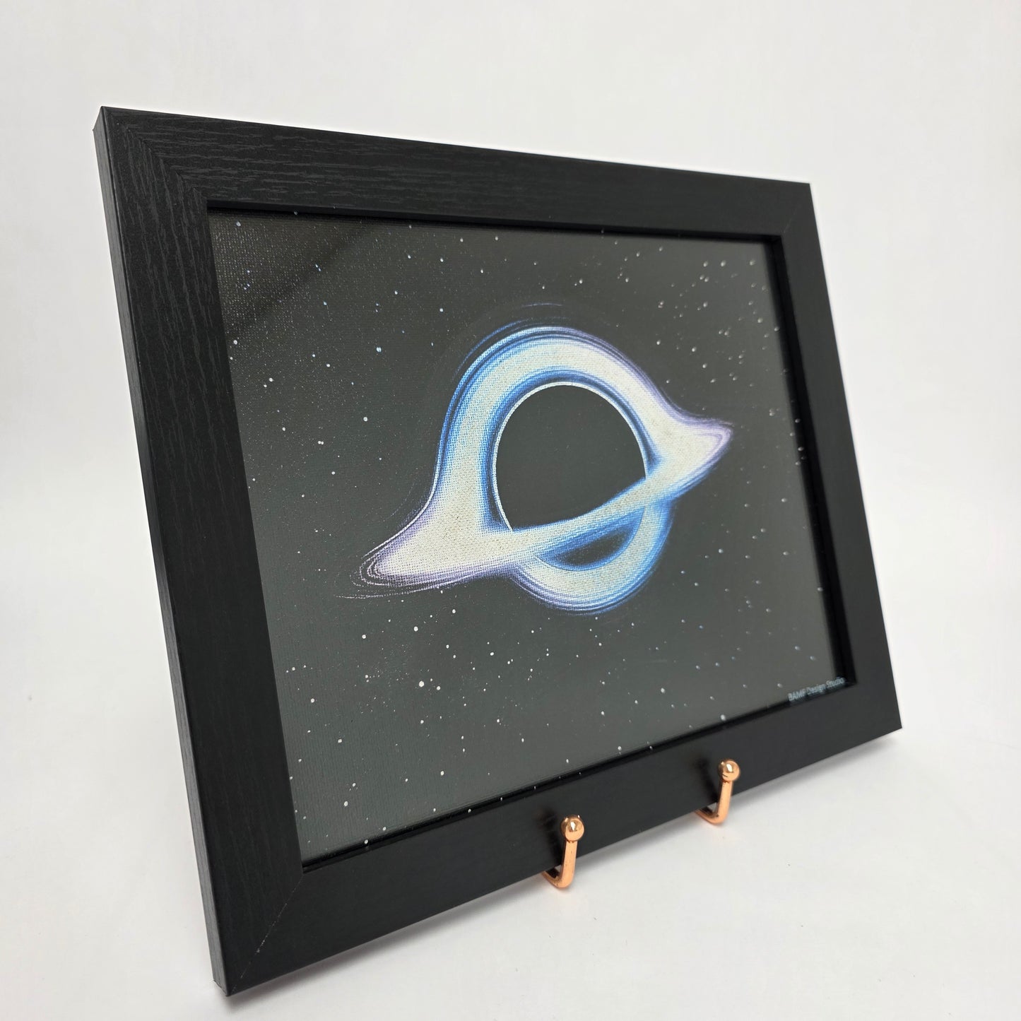 Black framed canvas print of a cosmic black hole surrounded by blue and purple hues. Black starry background.