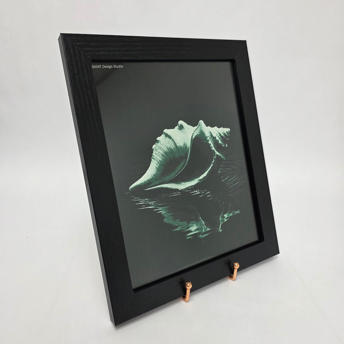 Black framed canvas print of a conch shell on water with water ripples around it. Black and green accents.