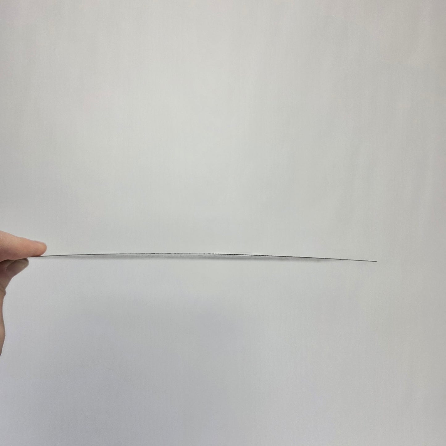 Long thin metal sign held by a hand against a plain background