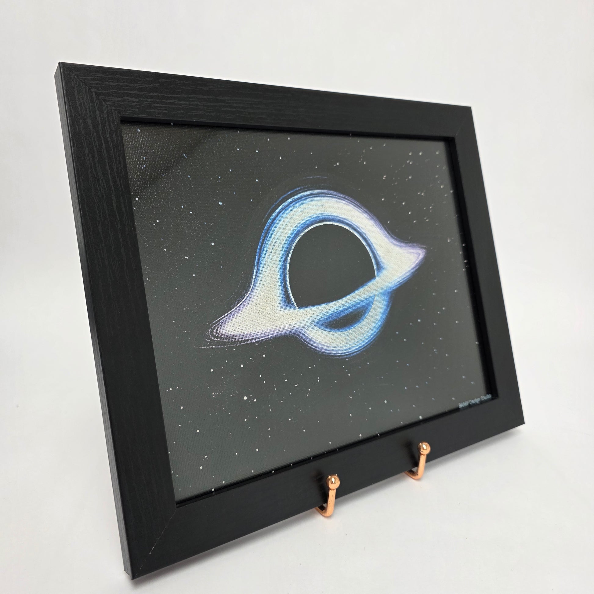 Black framed canvas print of a cosmic black hole surrounded by blue and purple hues. Black starry background.