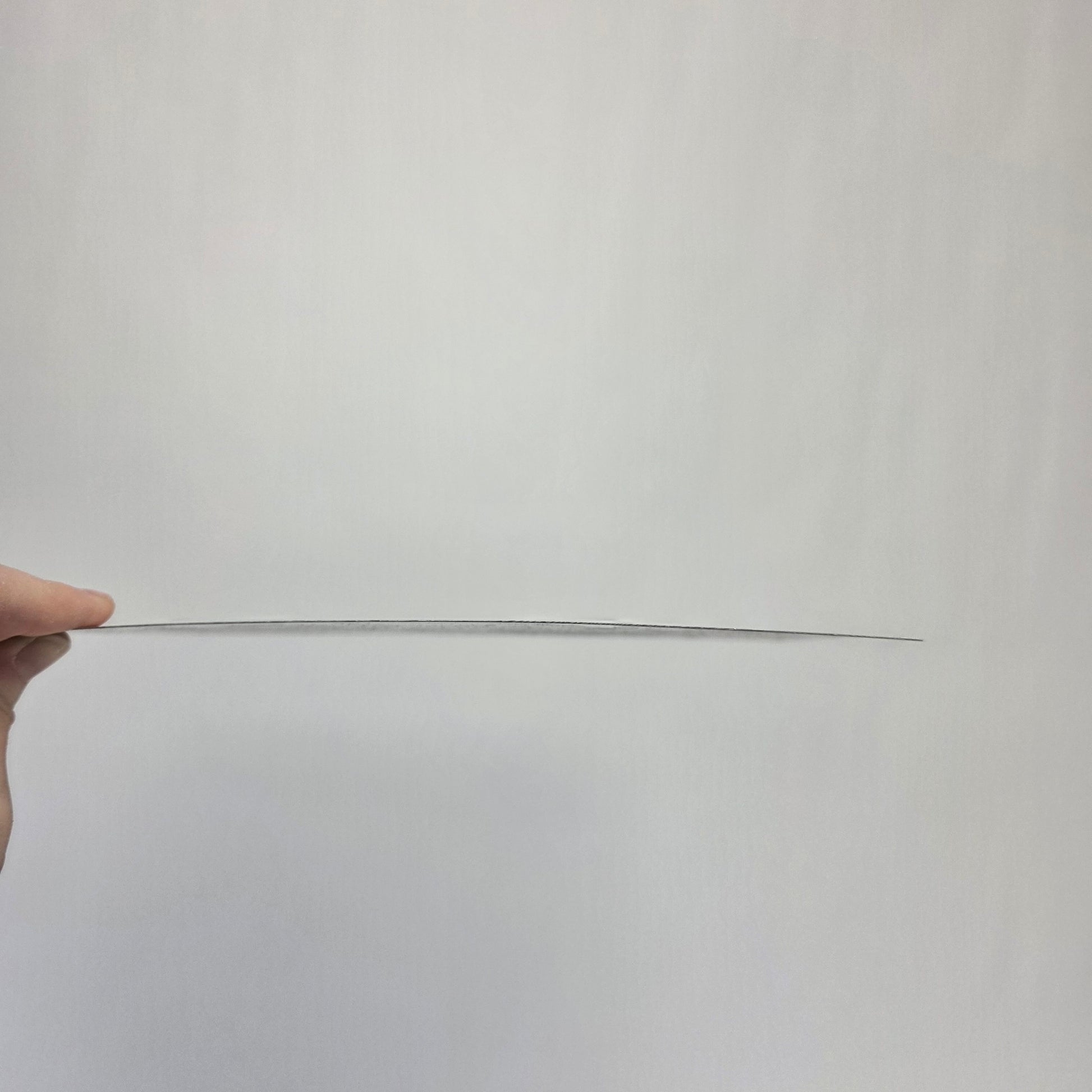 Long thin metal sign held by a hand against a plain background