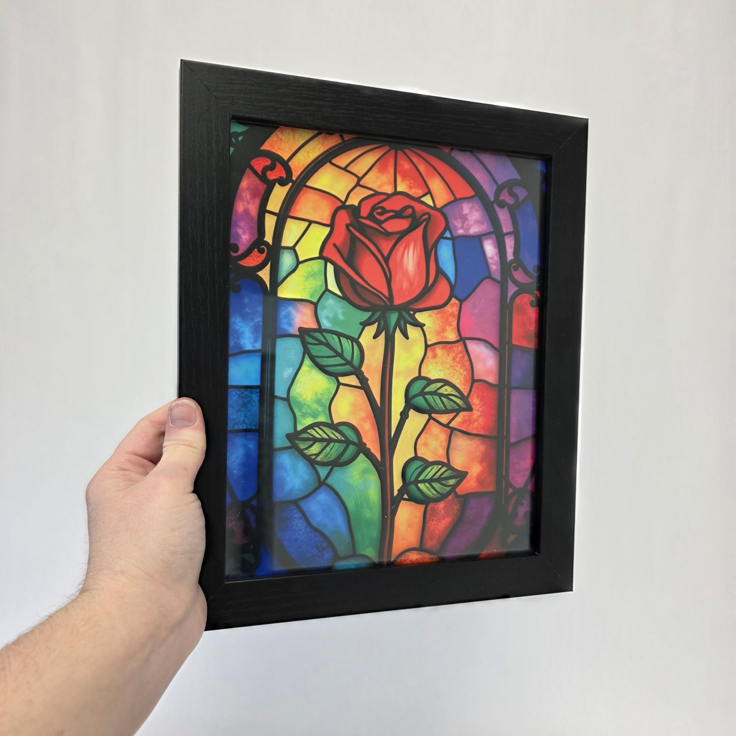 Framed stained glass artwork with a rose and leaves in front of a white background