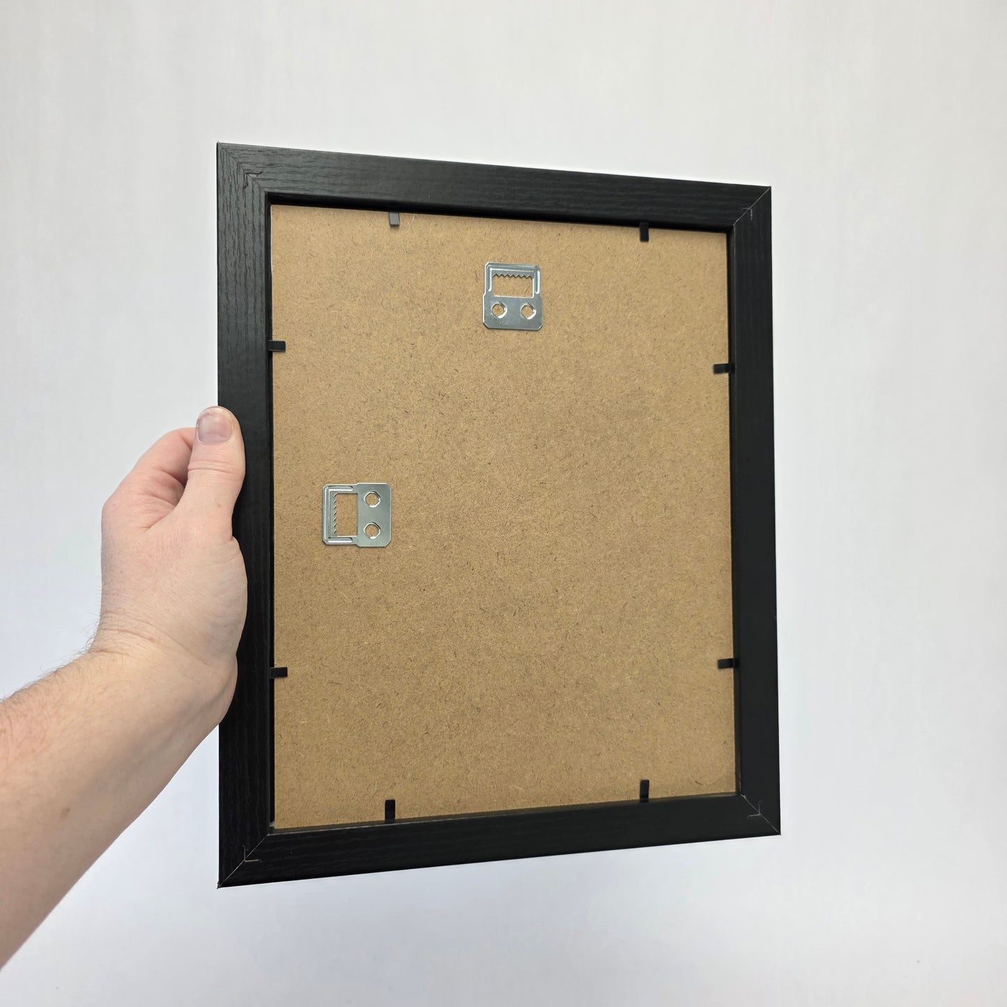 Hand holding a black picture frame with a white background