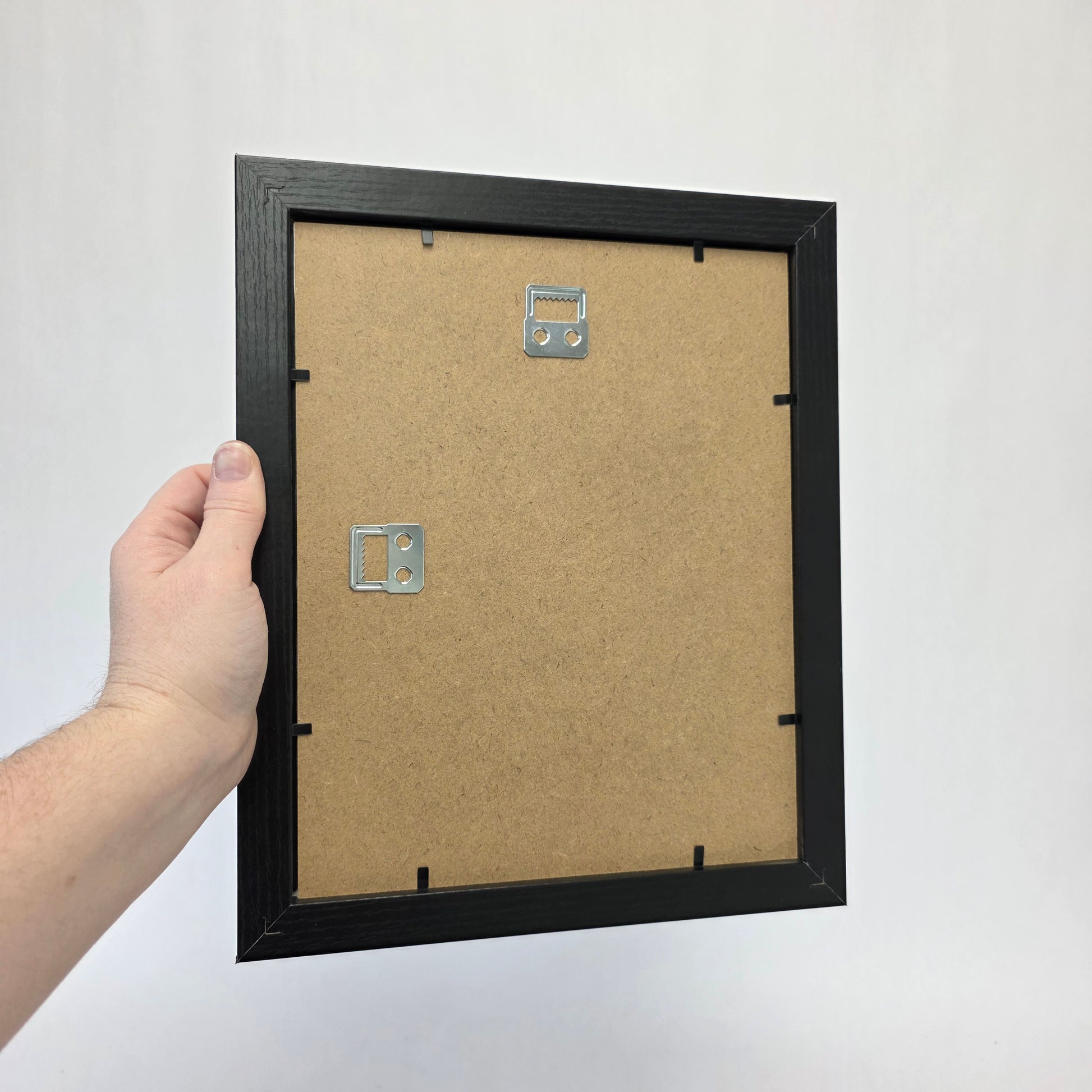 Hand holding a black picture frame with a white background