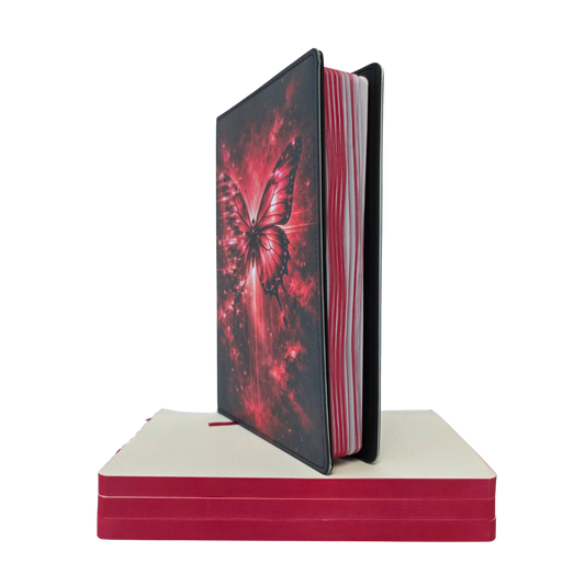 Notebook with butterfly design on cover on a white background, sitting on top of a stack of red paper.