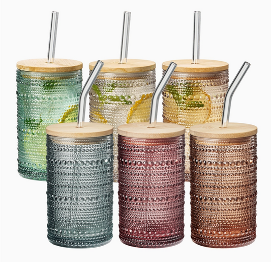 Six patterned glass tumblers with wooden lids and glass straws on a white background. Colors include Green, clear, light pink, blue, reddish purple, and orange.